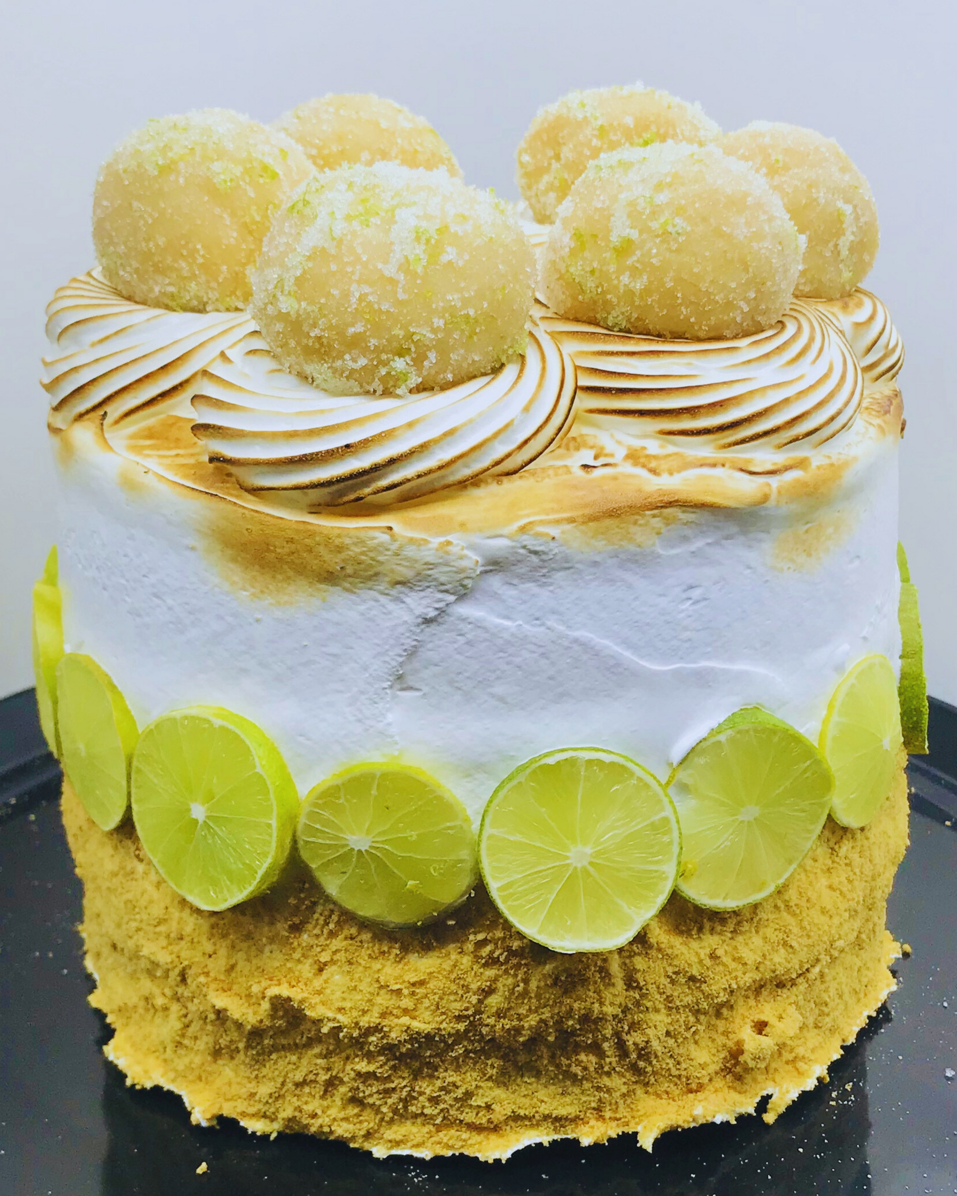 Cake with lemon curd filling, meringue, and lime slices on a white background